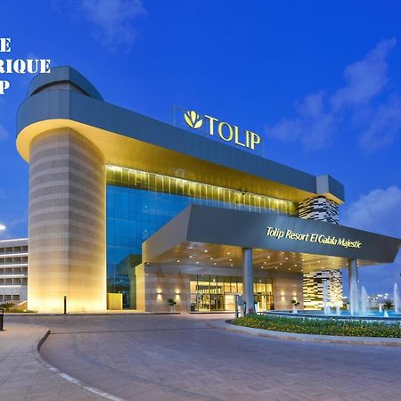 Tolip Resort El Galala Majestic Ain Sukhna Ngoại thất bức ảnh The photo shows a modern hotel building named "Tolip Resort & Spa," featuring a sleek architectural design with large glass windows. The hotel is illuminated against a twilight sky, showcasing its prominent signage. In the foreground, there is a well