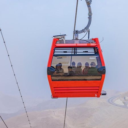 Tolip Resort El Galala Majestic Ain Sukhna Ngoại thất bức ảnh The photo shows a red gondola lift suspended in the air, traveling along cables. Inside the gondola, a group of people can be seen. The background features a hazy landscape, possibly mountains or hills, indicating an elevated area. The scene conveys 