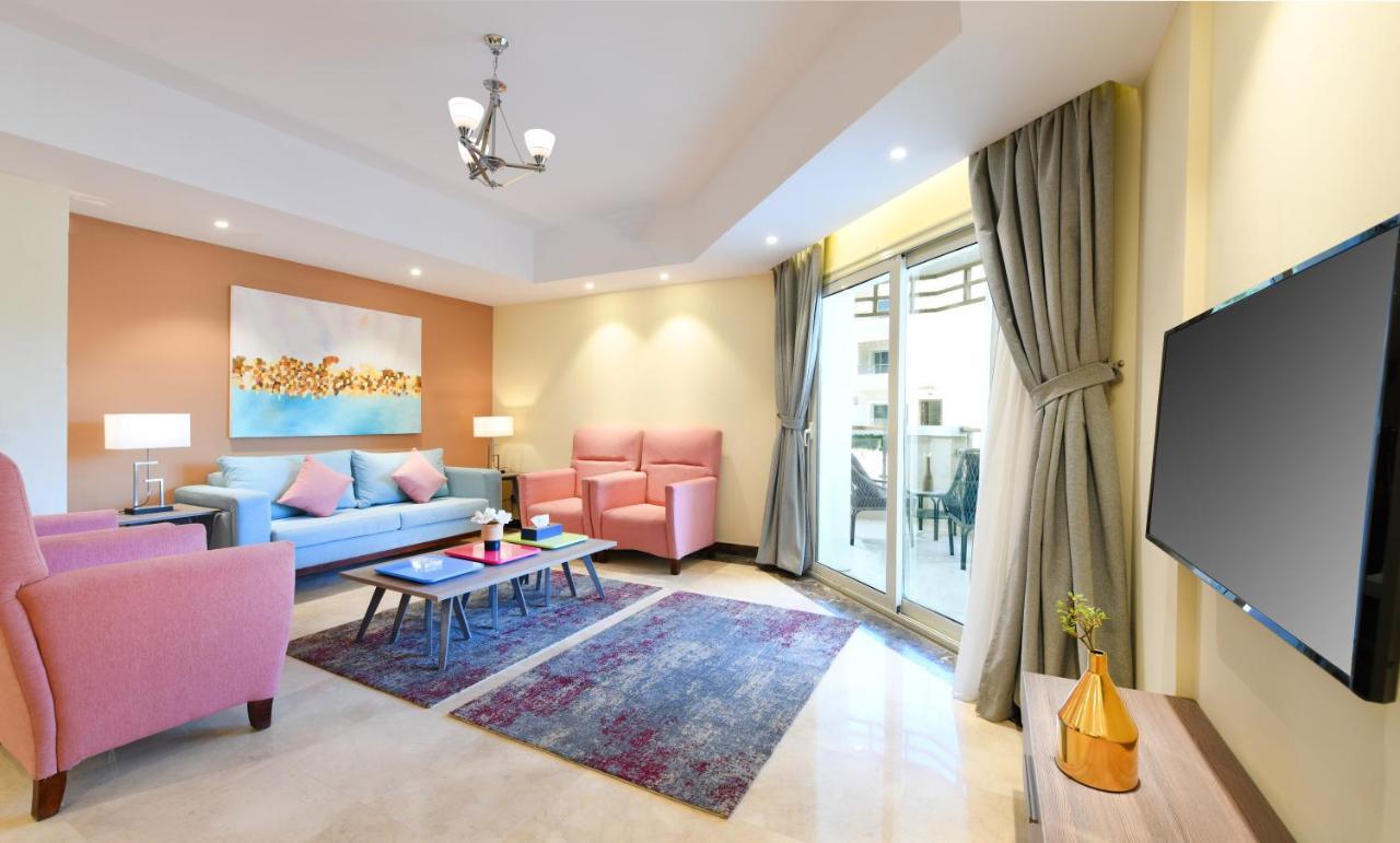 Tolip Resort El Galala Majestic Ain Sukhna Phòng bức ảnh The photo shows a modern living room that features a cozy and stylish design. There is a light blue sofa adorned with pastel pink cushions, accompanied by two pink armchairs. A coffee table sits in front, placed on a colorful area rug that adds warmt