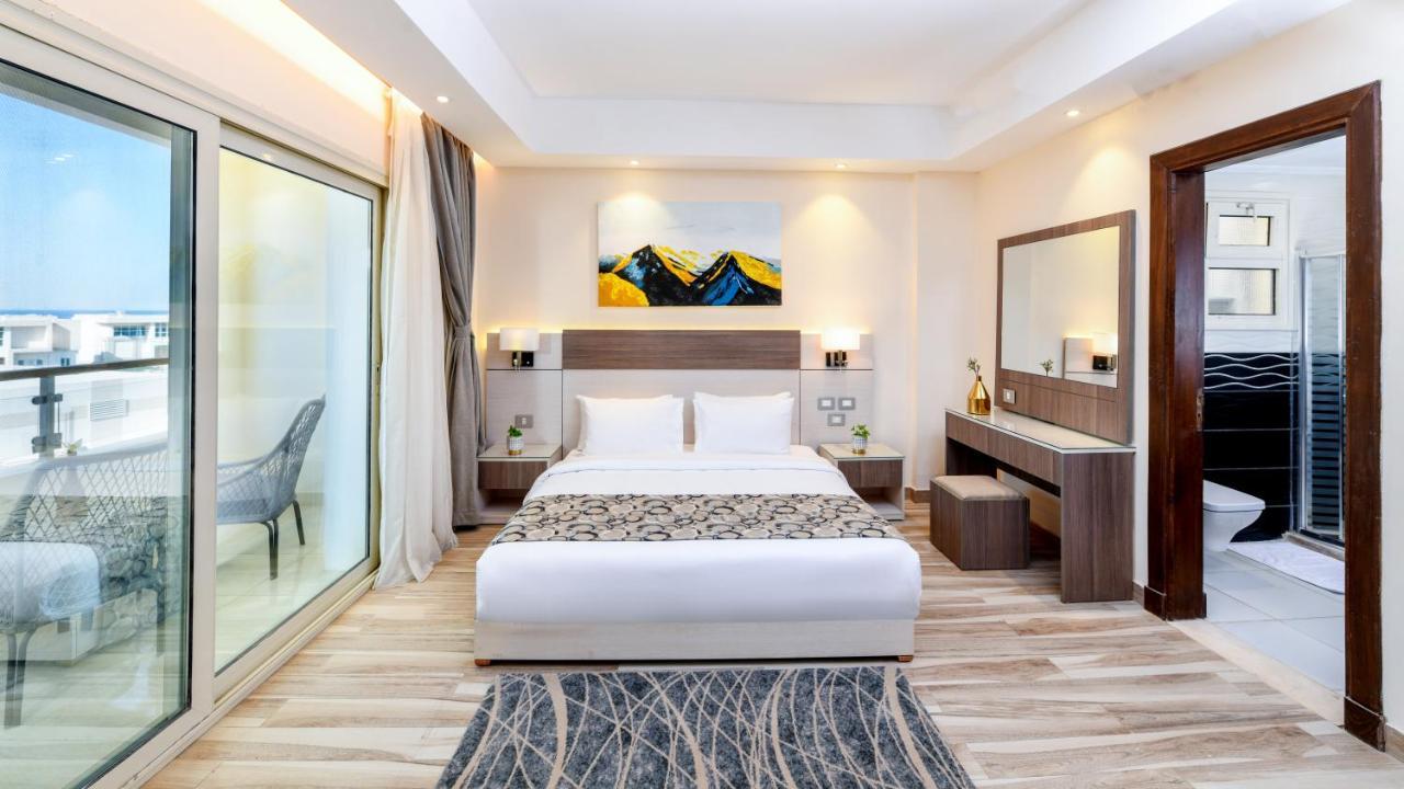 Tolip Resort El Galala Majestic Ain Sukhna Ngoại thất bức ảnh The photo shows a modern hotel room featuring a large bed with white linens and a decorative throw. The room has a neutral color palette, accented with warm lighting. There is a piece of artwork above the bed depicting mountains. To the left, there a