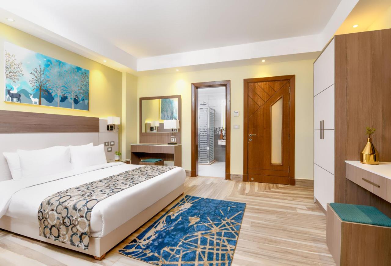 Tolip Resort El Galala Majestic Ain Sukhna Ngoại thất bức ảnh The photo shows a well-decorated hotel room. There is a large bed with white linens and a decorative throw blanket. The room features a wooden wardrobe and a bedside table with lamps. A colorful rug is placed on the floor, adding warmth to the space.