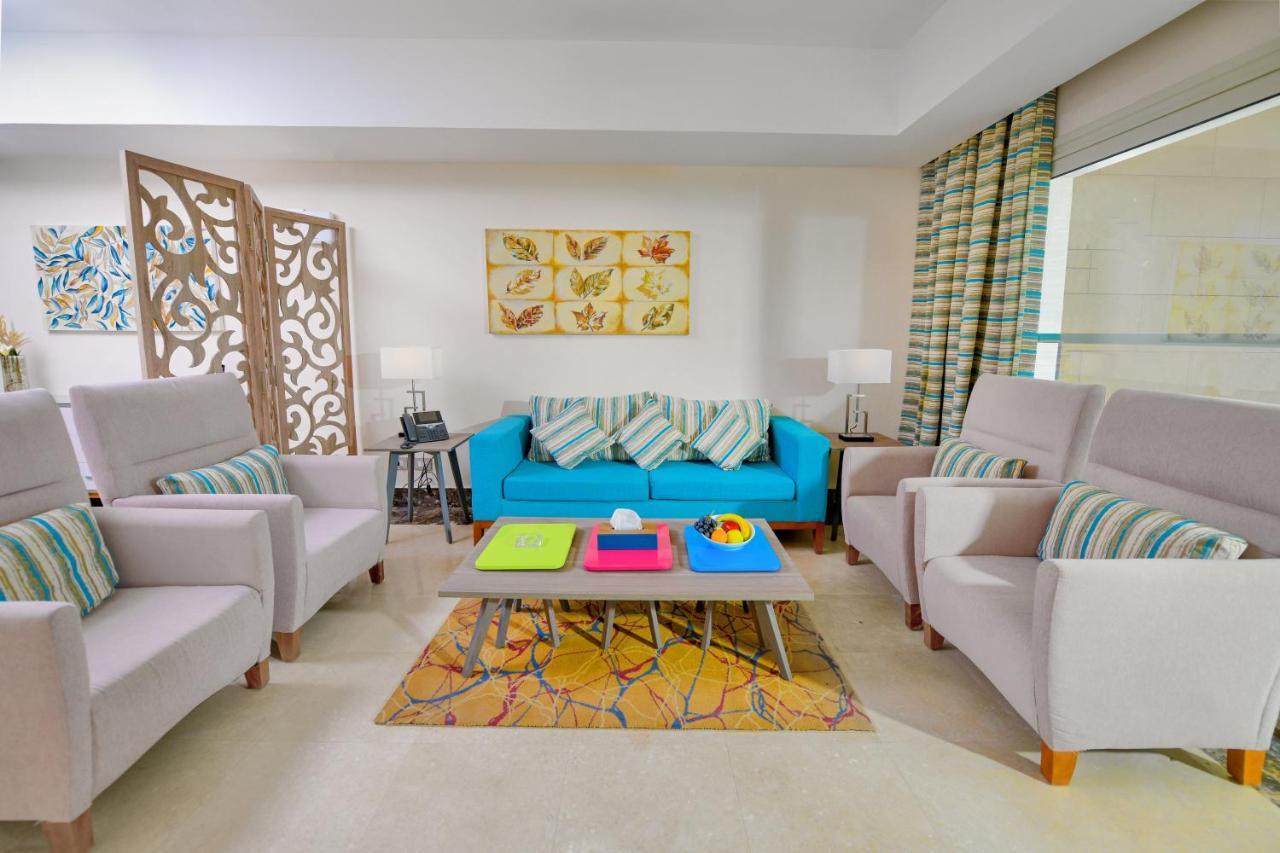 Tolip Resort El Galala Majestic Ain Sukhna Ngoại thất bức ảnh The photo shows a stylish and colorful living room. It features a bright blue sofa with patterned cushions, complemented by two light gray armchairs. In front of the sofa, there's a wooden coffee table with vibrant trays in pink, green, and yellow. A