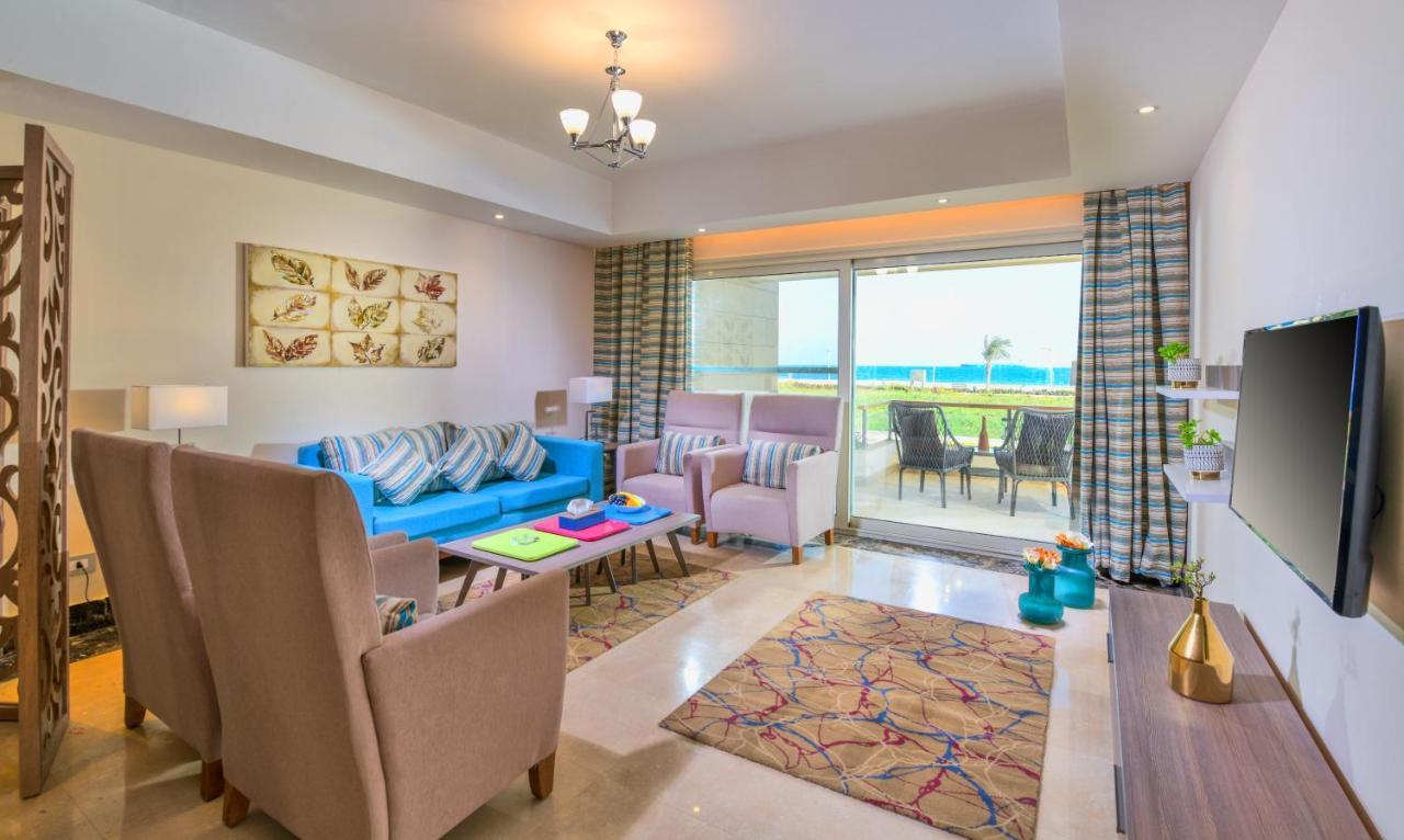 Tolip Resort El Galala Majestic Ain Sukhna Ngoại thất bức ảnh The photo shows a bright and modern living room. It features a blue sofa with decorative cushions, two light-colored armchairs, and a coffee table. A large area rug adds warmth to the space, which is decorated with a subtle pattern. The walls have so
