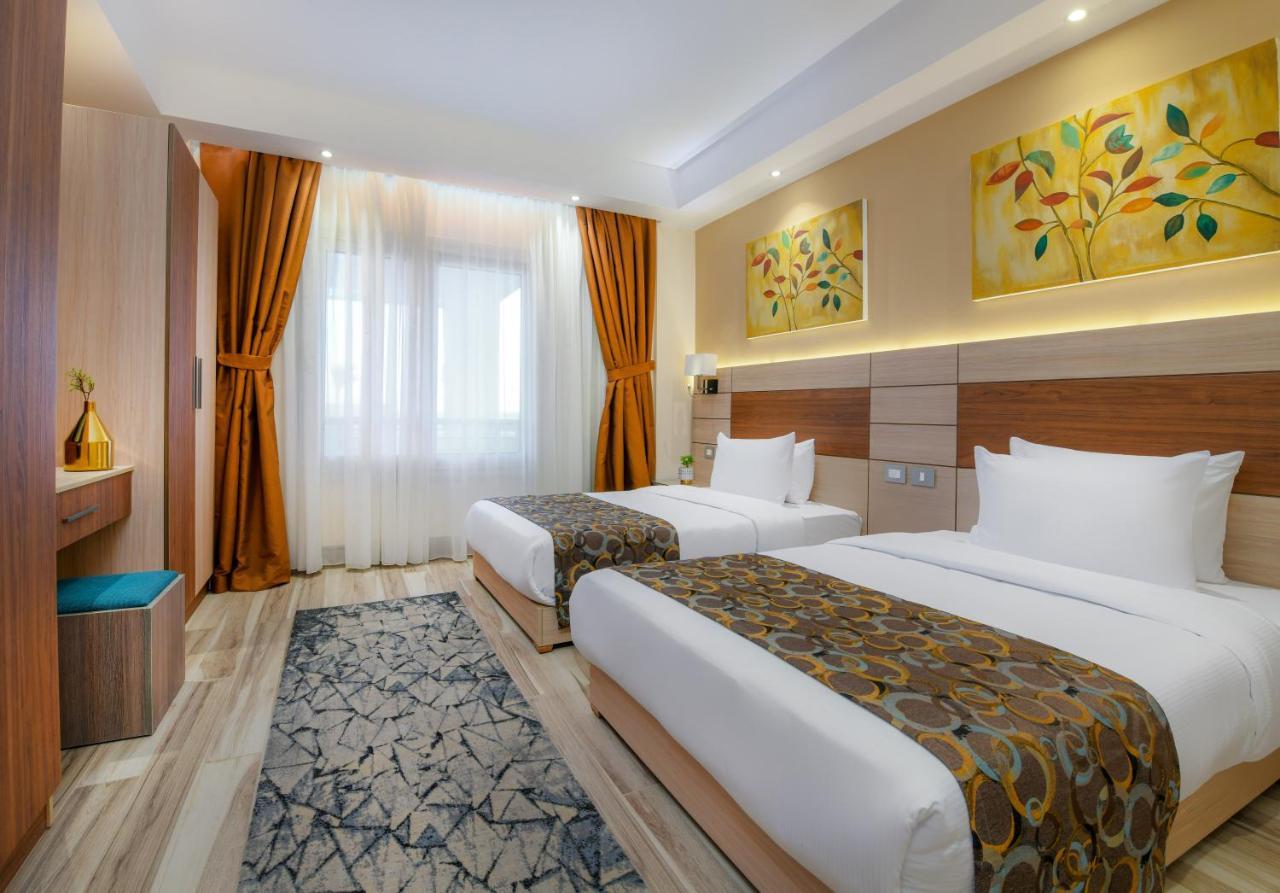 Tolip Resort El Galala Majestic Ain Sukhna Ngoại thất bức ảnh The photo shows a modern hotel room with two single beds, each covered with white linens and decorative brown bed throws. The walls are painted in warm colors, and there are two pieces of artwork featuring floral and leaf designs above the beds. The 