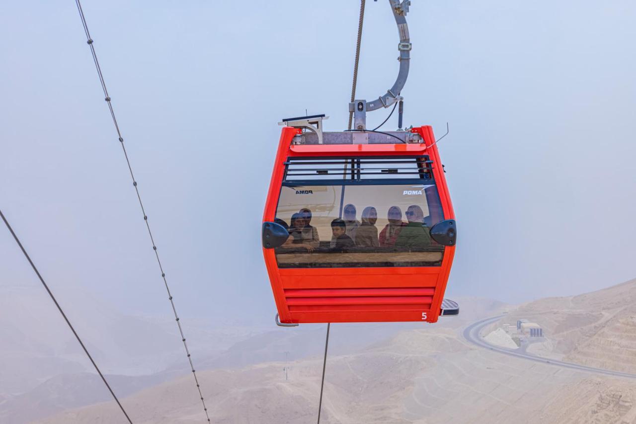 Tolip Resort El Galala Majestic Ain Sukhna Ngoại thất bức ảnh The photo shows a red gondola lift suspended in the air, traveling along cables. Inside the gondola, a group of people can be seen. The background features a hazy landscape, possibly mountains or hills, indicating an elevated area. The scene conveys 