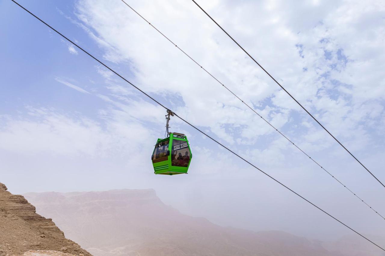 Tolip Resort El Galala Majestic Ain Sukhna Ngoại thất bức ảnh The photo shows a green cable car suspended in the air, traveling along overhead cables. The backdrop features a hazy landscape, likely mountainous or elevated terrain, with a cloudy sky. The scene suggests a scenic transportation method, possibly us
