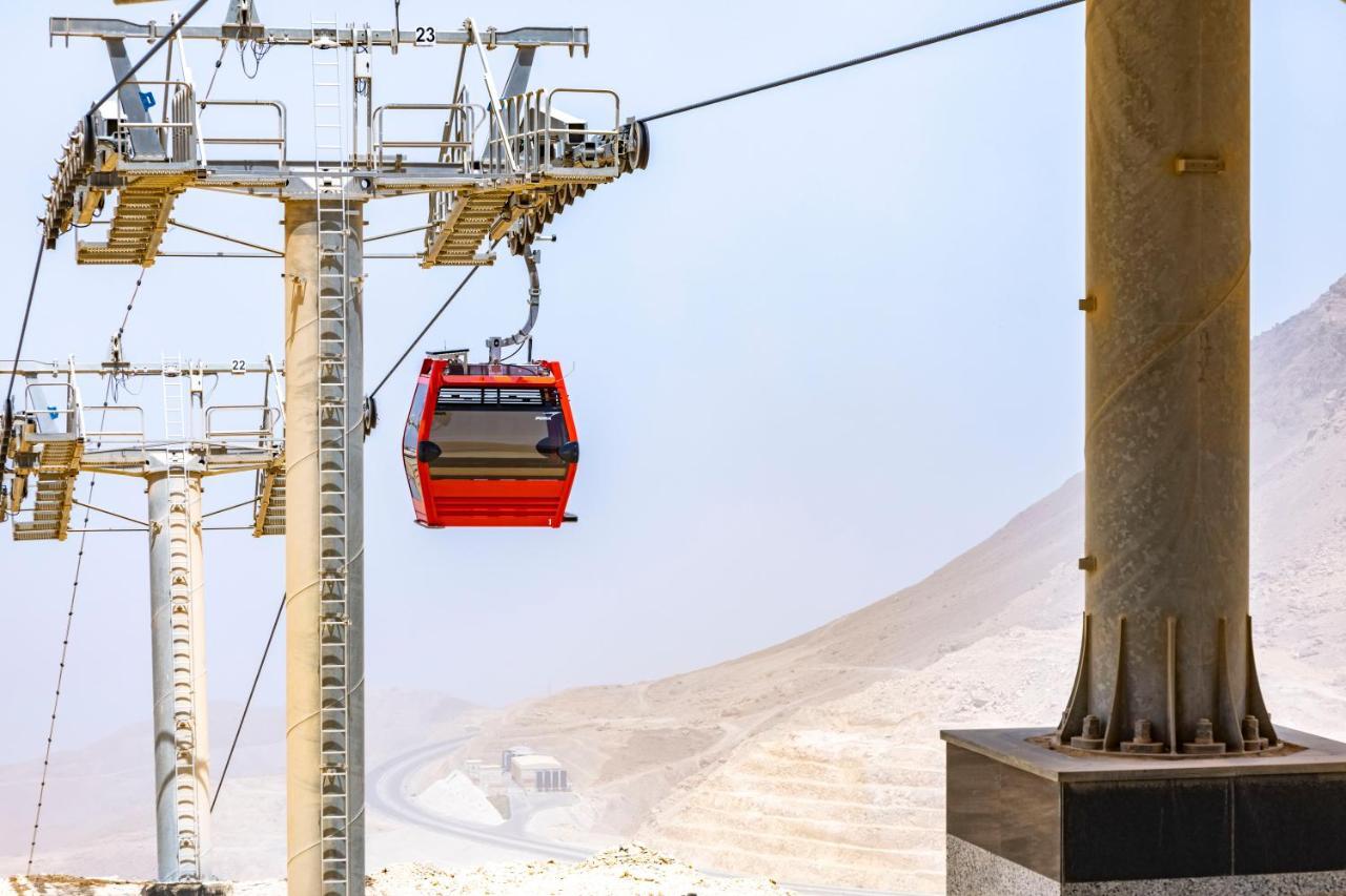 Tolip Resort El Galala Majestic Ain Sukhna Ngoại thất bức ảnh The photo shows a cable car system with a single red gondola suspended mid-air. It appears to be part of a larger cable car infrastructure, with metal pylons supporting the cables above. The background features a hazy landscape, likely characterized 