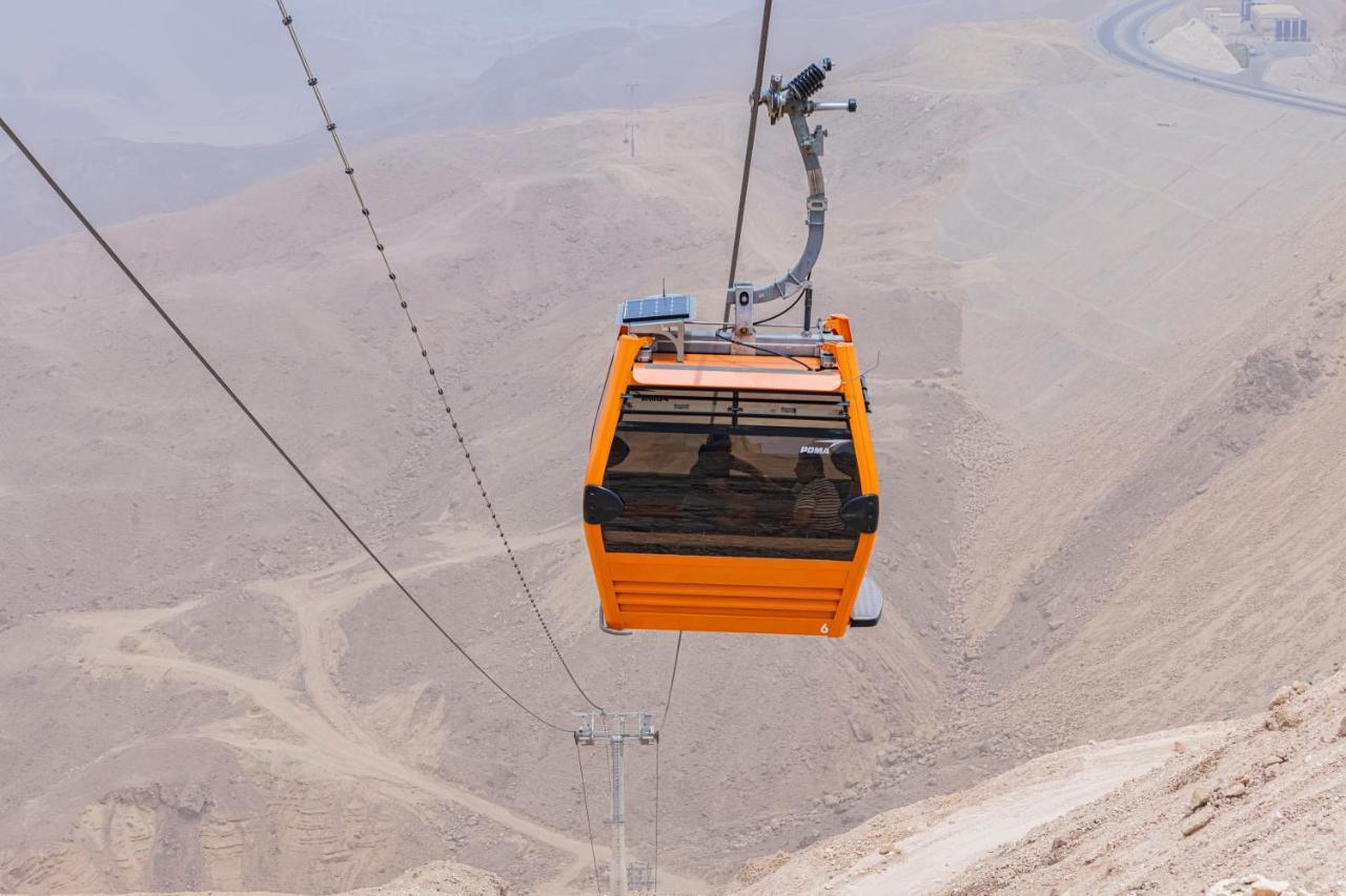 Tolip Resort El Galala Majestic Ain Sukhna Ngoại thất bức ảnh The photo shows an orange cable car suspended in the air, traveling along a set of cables. It appears to be located in a mountainous or hilly area, with rugged terrain and dry, rocky landscapes visible below. The background features slopes that seem 