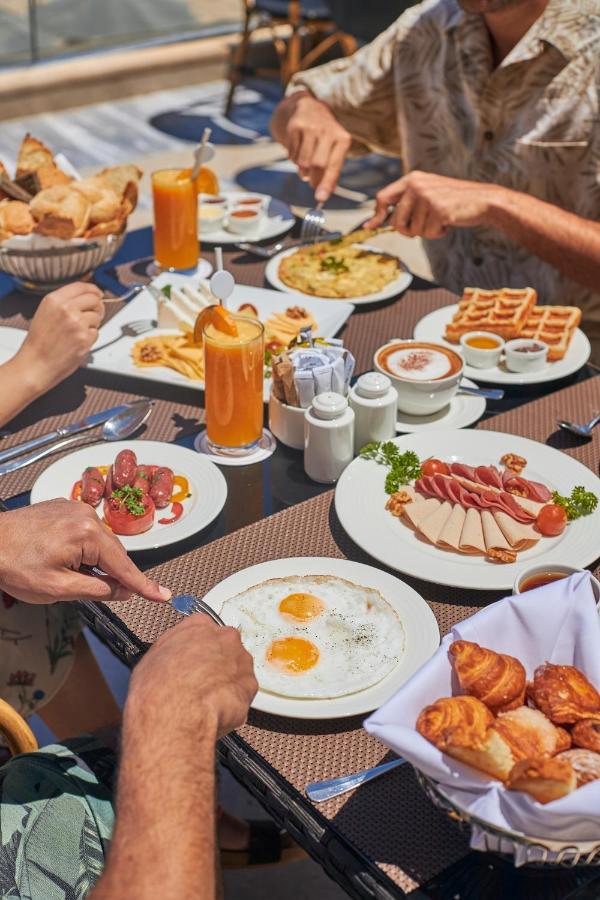 Tolip Resort El Galala Majestic Ain Sukhna Ngoại thất bức ảnh The photo features a spread of breakfast dishes on a table. There are two sunny-side-up eggs on one plate, surrounded by various food items, including slices of ham, sausages, and fresh tomatoes. Another plate holds a serving of waffles. A bowl with 