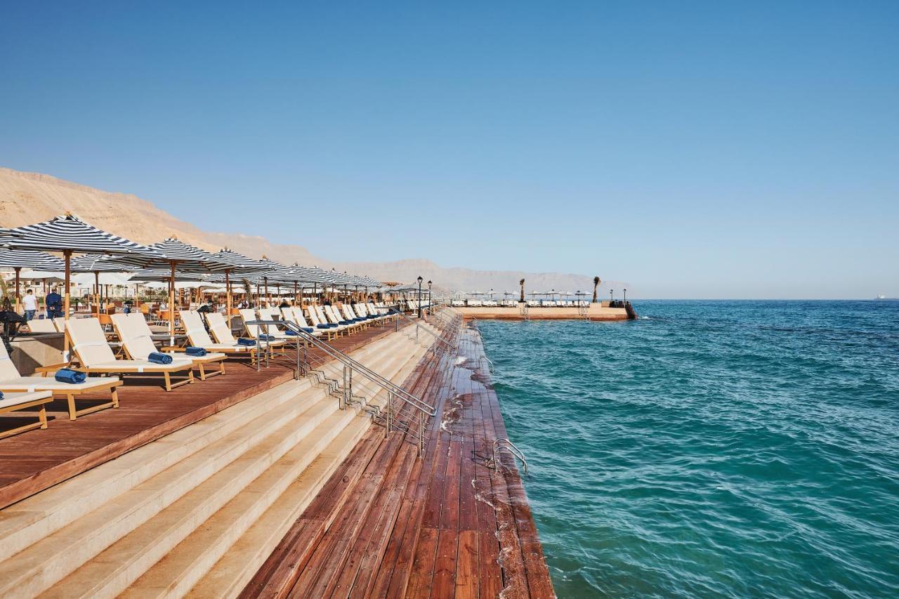 Tolip Resort El Galala Majestic Ain Sukhna Ngoại thất bức ảnh The photo shows a seaside area featuring a wooden deck that extends into the water. On the left side, there are several lounge chairs arranged neatly under shade structures, suggesting a relaxing atmosphere. The ocean is visible in the foreground, wi