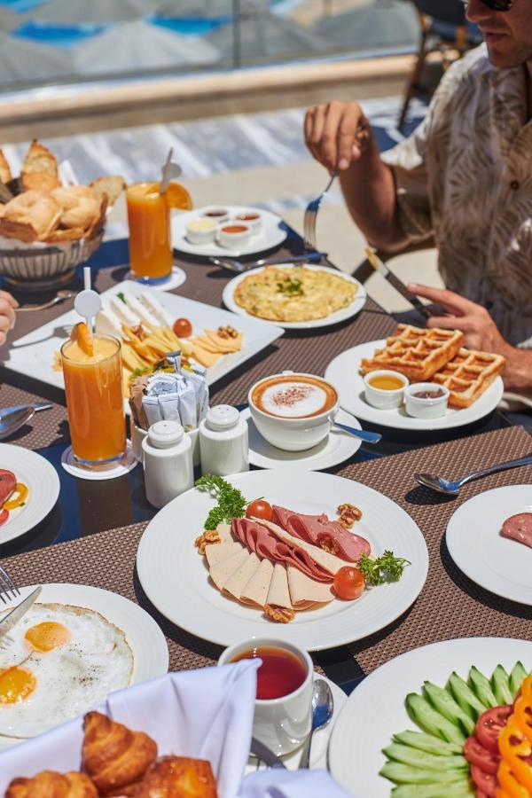Tolip Resort El Galala Majestic Ain Sukhna Ngoại thất bức ảnh The photo shows a breakfast spread laid out on a table. There are several plates with a variety of food items, including:

1. **Sliced Cold Cuts**: A plate featuring various cold meats, accompanied by garnishes like cherry tomatoes and lettuce.
2. **