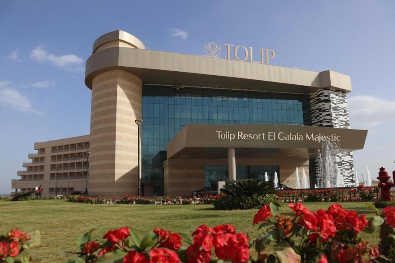 Tolip Resort El Galala Majestic Ain Sukhna Ngoại thất bức ảnh The photo shows a modern hotel building named "Tolip Resort El Galala Majestic." The structure features a distinctive architectural design with large glass windows and a prominent entrance. Surrounding the building are well-maintained lawns and vibra