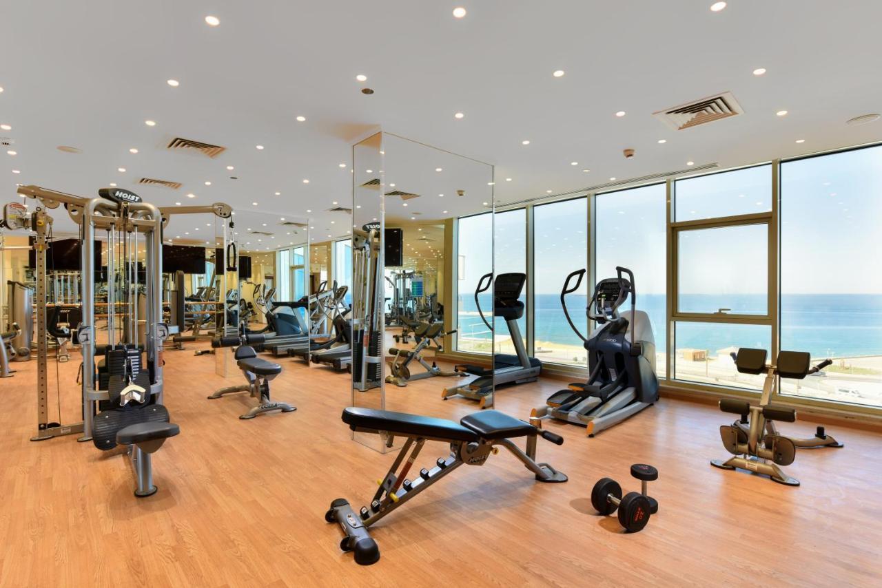 Tolip Resort El Galala Majestic Ain Sukhna Ngoại thất bức ảnh The photo shows a modern gym interior with a variety of fitness equipment. There are cardio machines like treadmills and ellipticals, along with strength training equipment such as free weights and benches. The gym features large windows that offer a