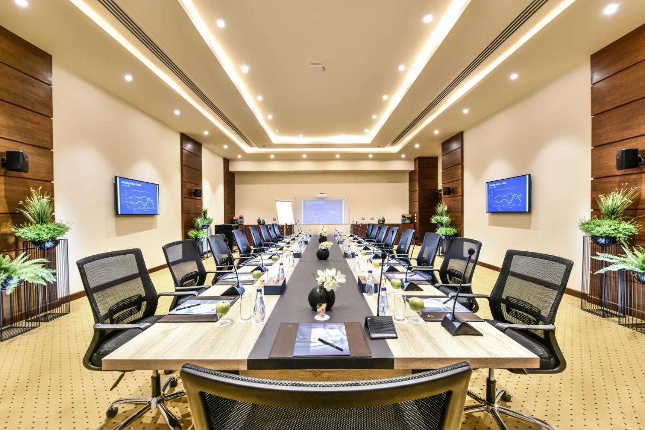 Tolip Resort El Galala Majestic Ain Sukhna Ngoại thất bức ảnh The photo shows a modern conference room designed for meetings. It features a long rectangular table at the center, surrounded by ergonomic black chairs. The room is well-lit with ceiling lights and has a neutral color scheme. There are two large scr