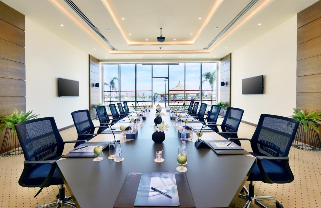 Tolip Resort El Galala Majestic Ain Sukhna Ngoại thất bức ảnh The image shows a modern conference room with a large, dark rectangular table surrounded by ergonomic black chairs. The room features large windows that allow natural light to enter and provide a view of the outdoors, including some greenery. On the 