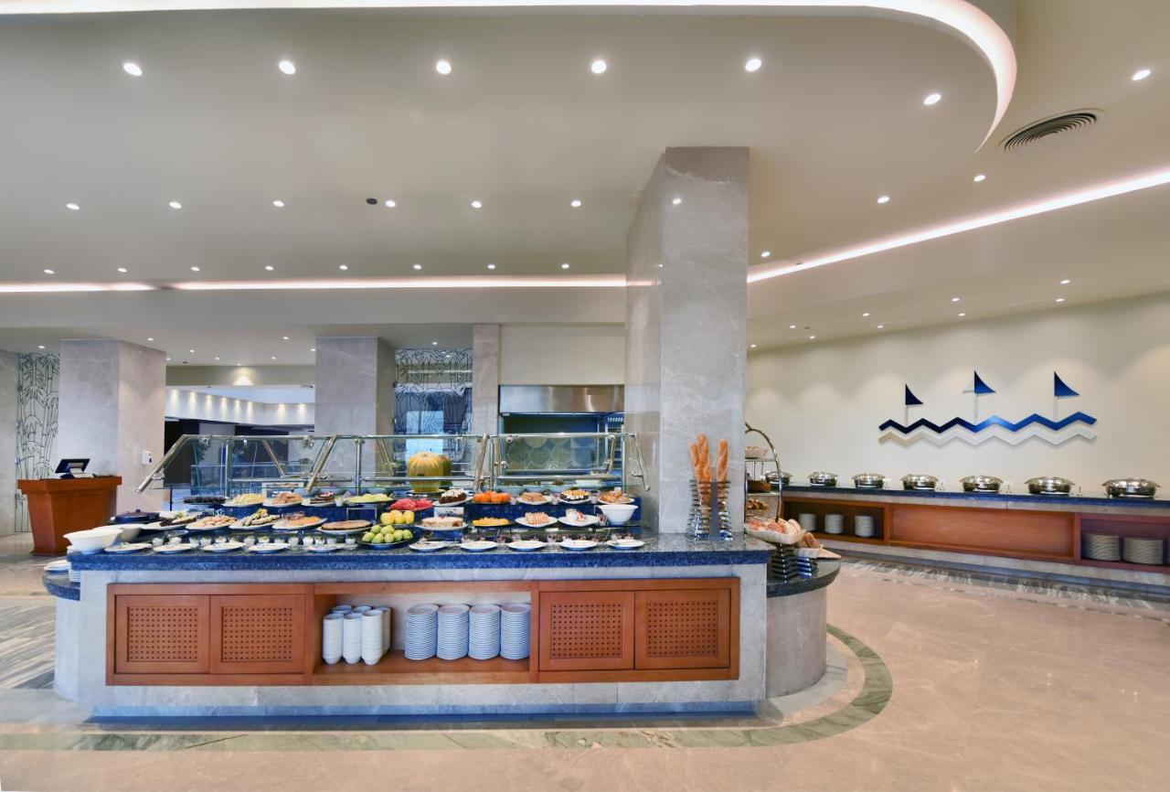 Tolip Resort El Galala Majestic Ain Sukhna Ngoại thất bức ảnh The image shows a buffet-style dining area in a restaurant or hotel. There are several food stations with a variety of dishes displayed, including fruits, salads, and other food items. The layout features a large, central island with a wooden base an