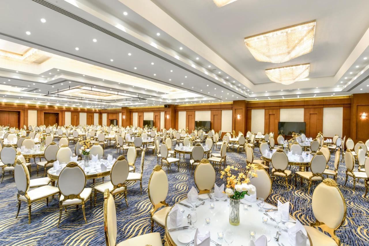 Tolip Resort El Galala Majestic Ain Sukhna Ngoại thất bức ảnh The photo shows a spacious and elegantly decorated banquet hall. The room features numerous round dining tables, each set with white tablecloths and adorned with decorative centerpieces, likely flowers. The chairs surrounding the tables have a luxuri